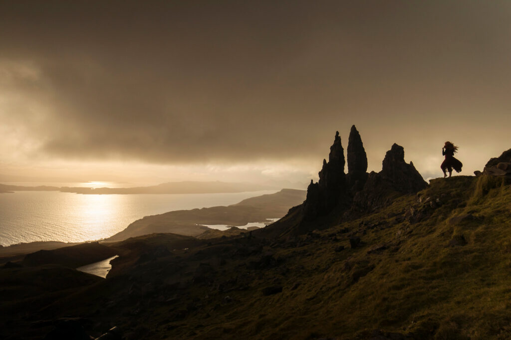 Dramatic landscape view of the Old Man of Storr at sunrise on the Isle of Skye, with warm light over the coastline and rocky pinnacles.