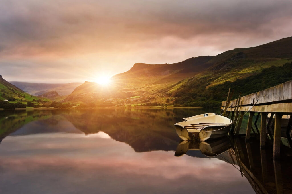 Sunrise over a calm lake in the Brecon Beacons, reflecting surrounding hills and moorland during a peaceful Wales campervan road trip.