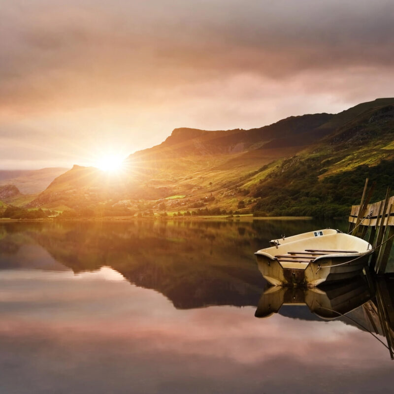 Sunrise over a calm lake in the Brecon Beacons, reflecting surrounding hills and moorland during a peaceful Wales campervan road trip.