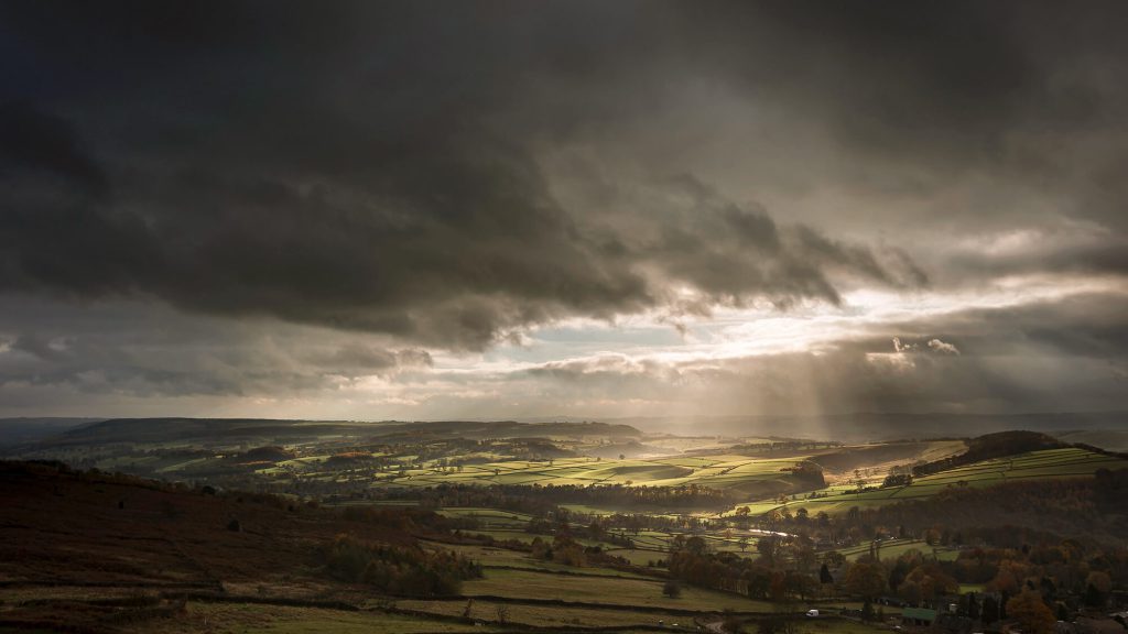 Dramatic storm clouds breaking over rolling Peak District hills with sunlight shining through
