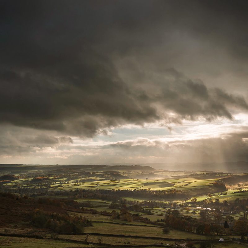 Dramatic storm clouds breaking over rolling Peak District hills with sunlight shining through