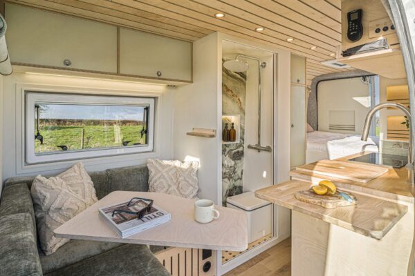 Campervan kitchen and seating area with light wood ceiling and Scandinavian-style cabinetry.
