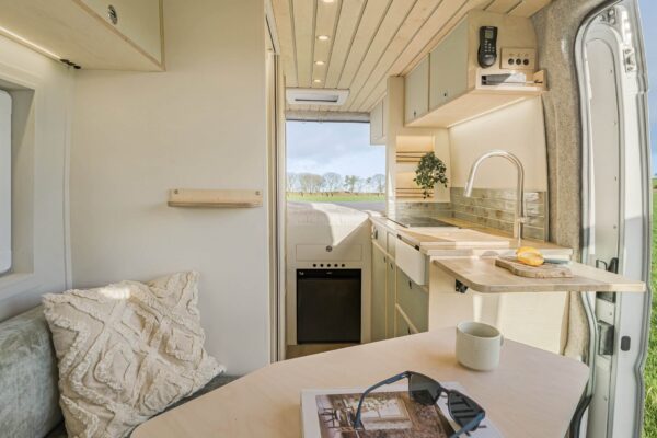 Wide view of campervan kitchen and living space with light cabinetry and uncluttered layout.