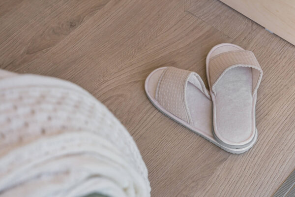 Campervan bed area detail with soft bedding and neutral-toned slippers on wood floor.