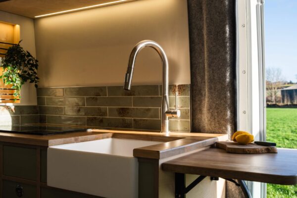 Campervan kitchen sink and tap detail with warm lighting and minimalist worktop.