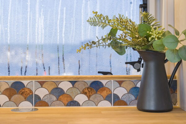 Campervan window ledge detail with tiled splashback and plant in natural light.