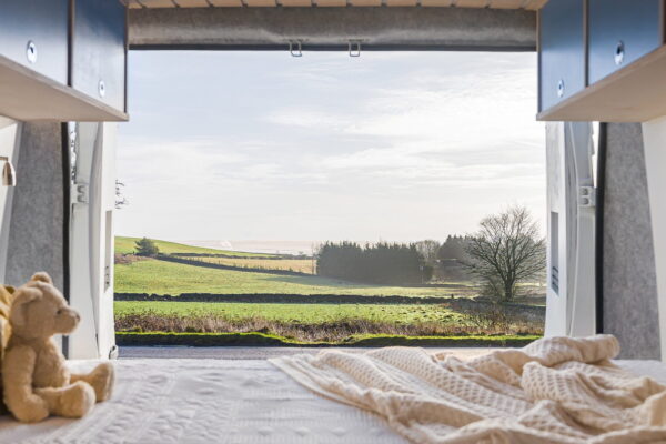View from campervan bed looking out through rear doors to open countryside.
