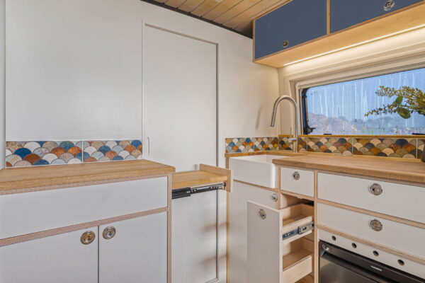Compact campervan kitchen with slim drawers, pale worktop and window above.