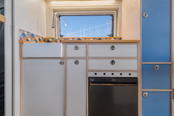 Campervan kitchen front view with oven, drawers and light wood cabinetry.