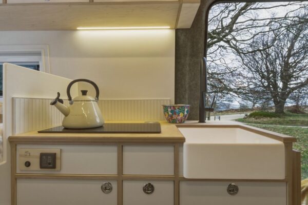 Campervan kitchen cabinetry with soft LED lighting and ceramic sink