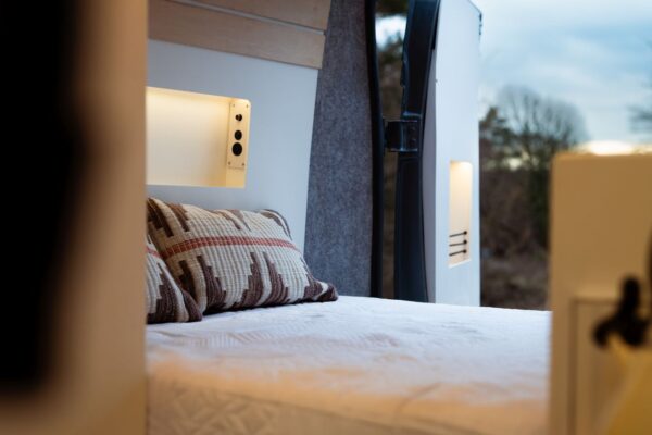 Rear sleeping area inside a Bhode campervan with natural wood cabinetry and window view