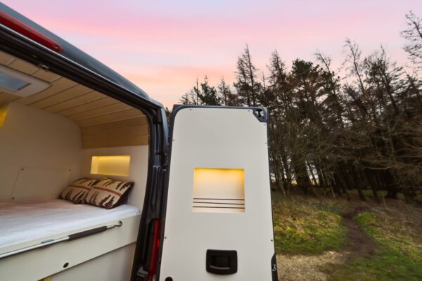 Exterior rear view of a Bhode campervan conversion with rear doors open and warm interior lighting at dusk