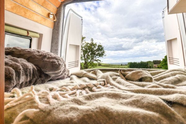 Fixed rear campervan bed with panoramic countryside views through open rear doors