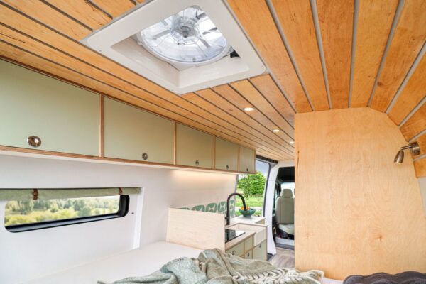 Luxury campervan interior with fixed bed, oak ceiling and roof ventilation