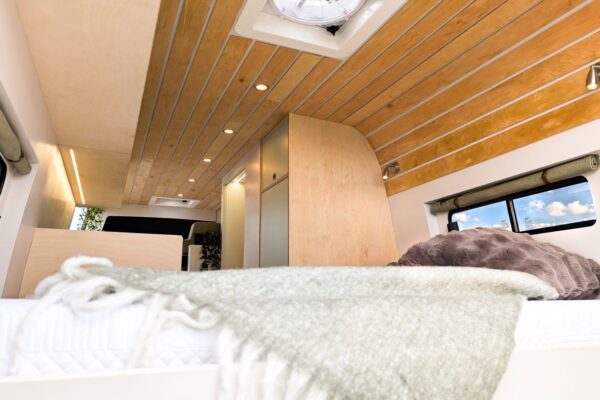 Fixed rear bed beneath oak slatted ceiling in a handcrafted campervan conversion