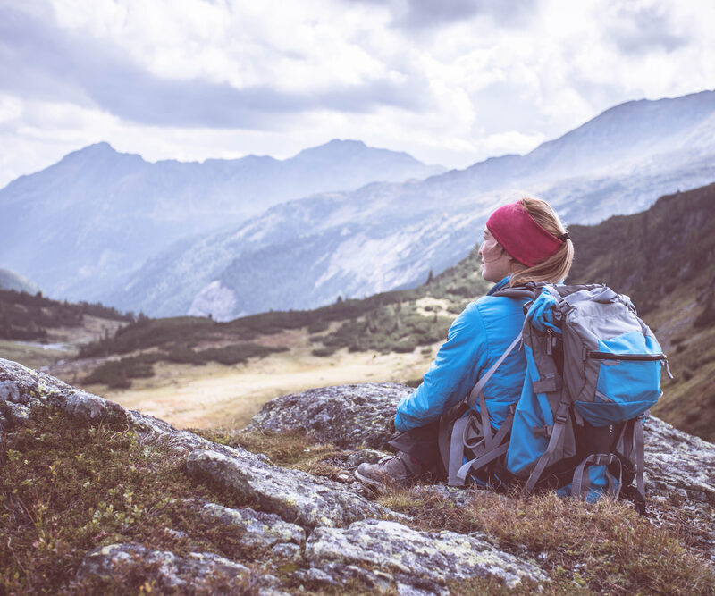 Woman with a backpack overlooking a mountain valley during a solo hiking adventure, ideal for campervan travel in the UK and Europe.