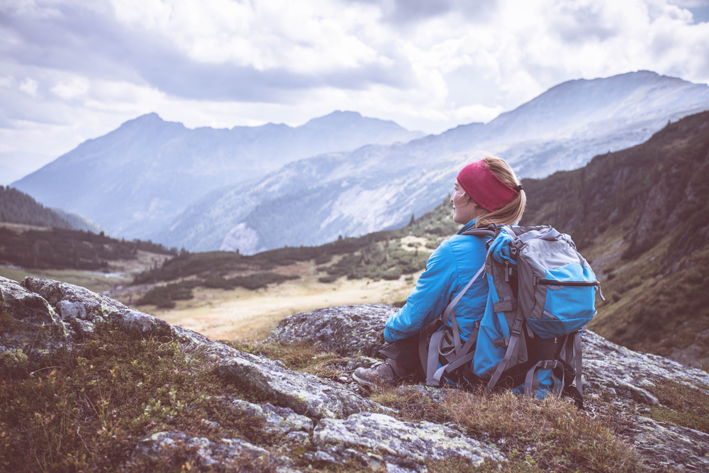 Woman with a backpack overlooking a mountain valley during a solo hiking adventure, ideal for campervan travel in the UK and Europe.